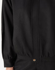 Modelo usando casaco preto com punhos largos e barra elástica, look completo com shorts pretos e mocassim - caimento estruturado