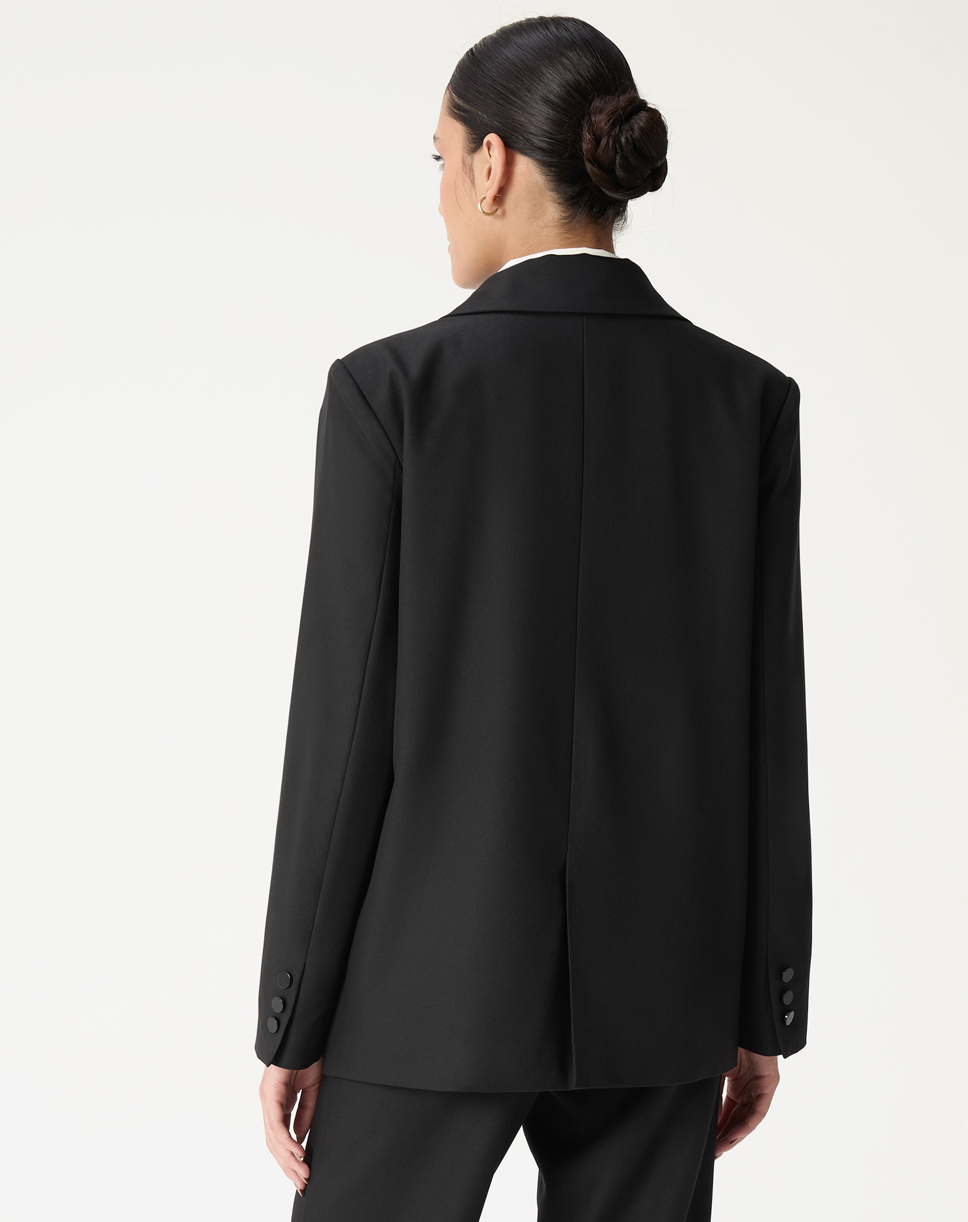 Vista traseira do blazer oversized preto mostrando costura central e fenda única, caimento alongado.
