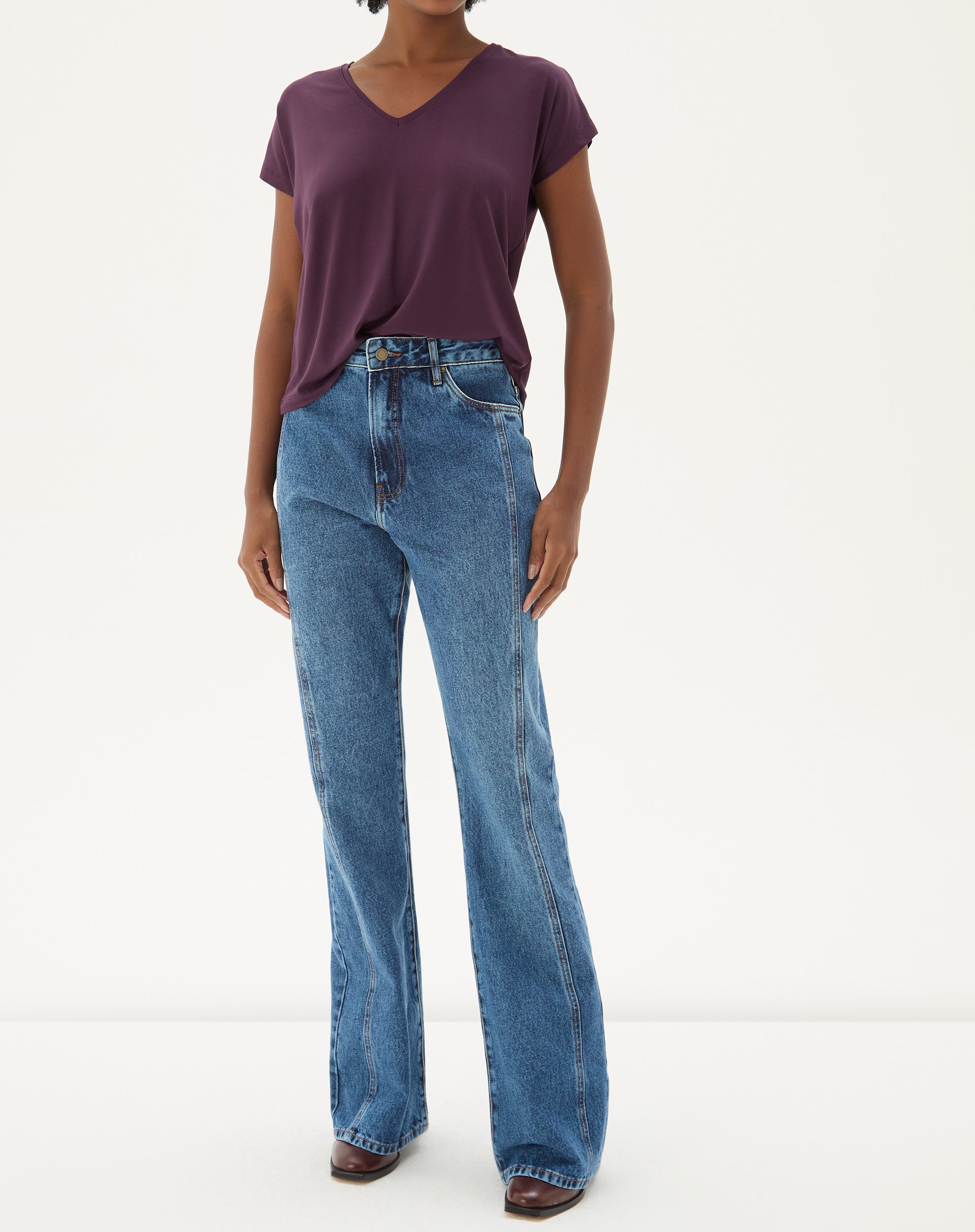 Modelo vestindo calça jeans flare azul médio com blusa roxa, vista frontal.