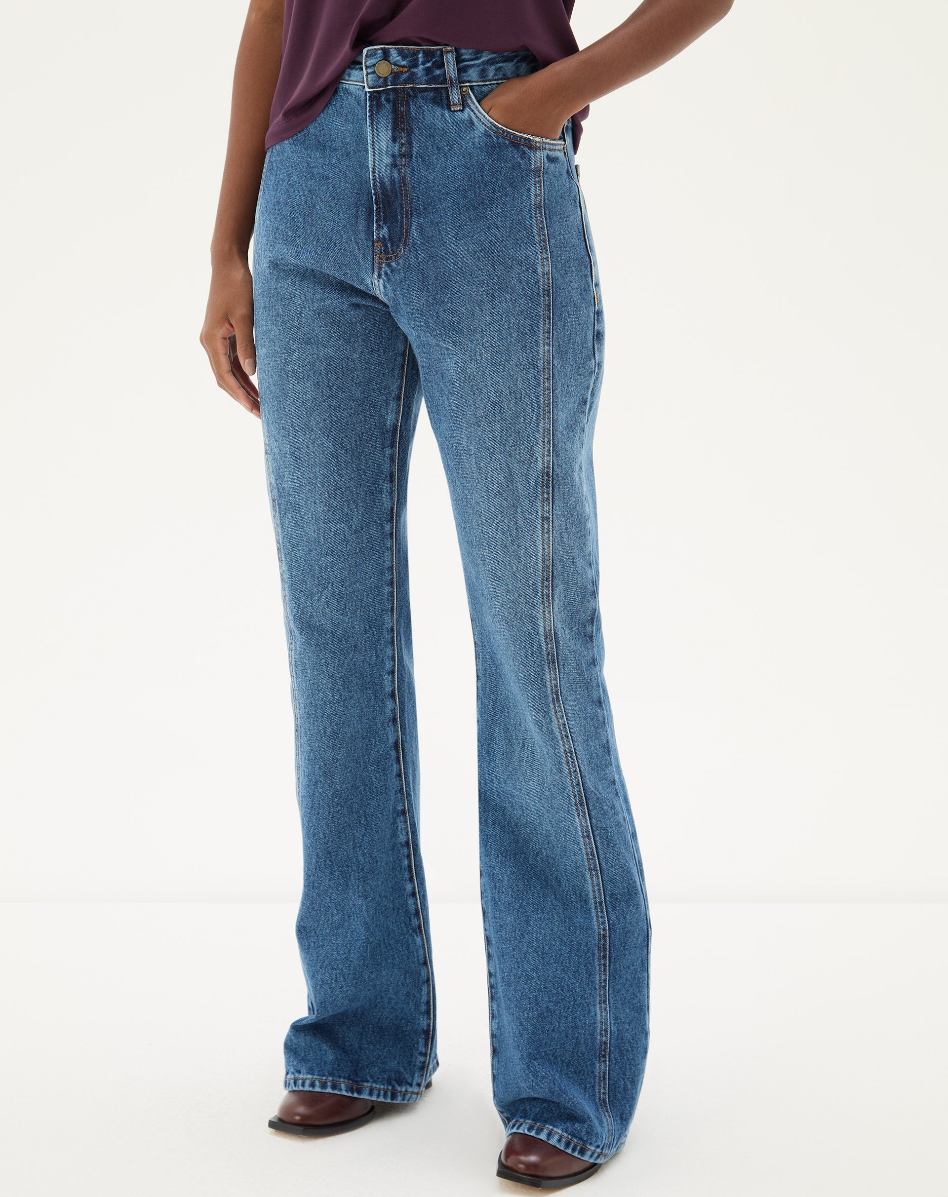 Vista frontal da calça jeans flare azul médio com blusa roxa.