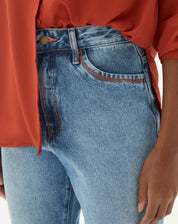 Detalhe do cós e fechamento da calça jeans azul claro.