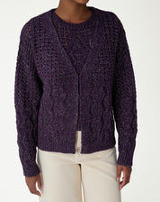 Close-up do decote V e abertura frontal do cardigan tricot roxo em fundo branco, mostrando a trama do ponto.