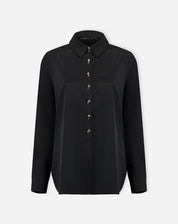 Look completo: modelo com camisa preta alongada por baixo de blazer preto e calça jeans de perna larga, proposta de styling